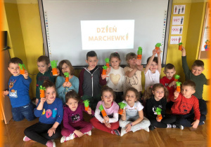 Dzieci z wykonanymi przez siebie marchewkami na tle napisu Dzień Marchewki